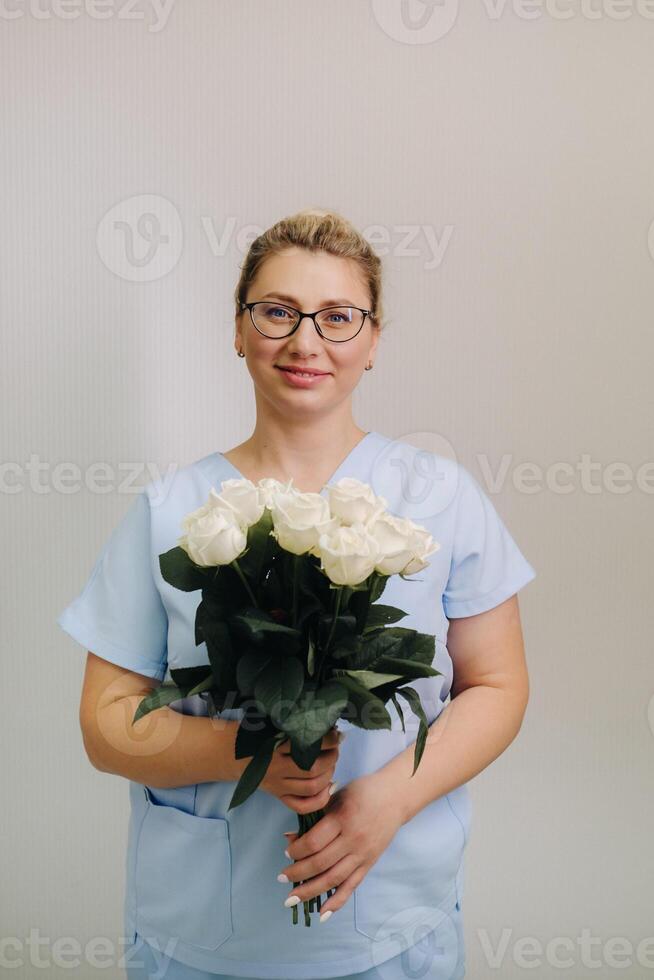 A female doctor in a blue robe with a bouquet of white roses in her hands photo