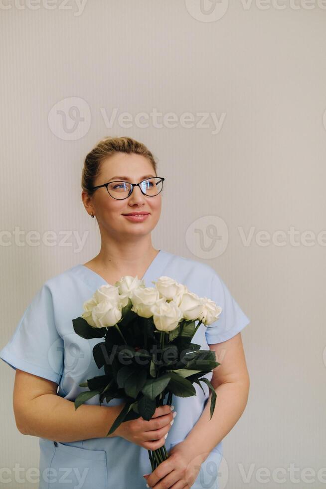A female doctor in a blue robe with a bouquet of white roses in her hands photo
