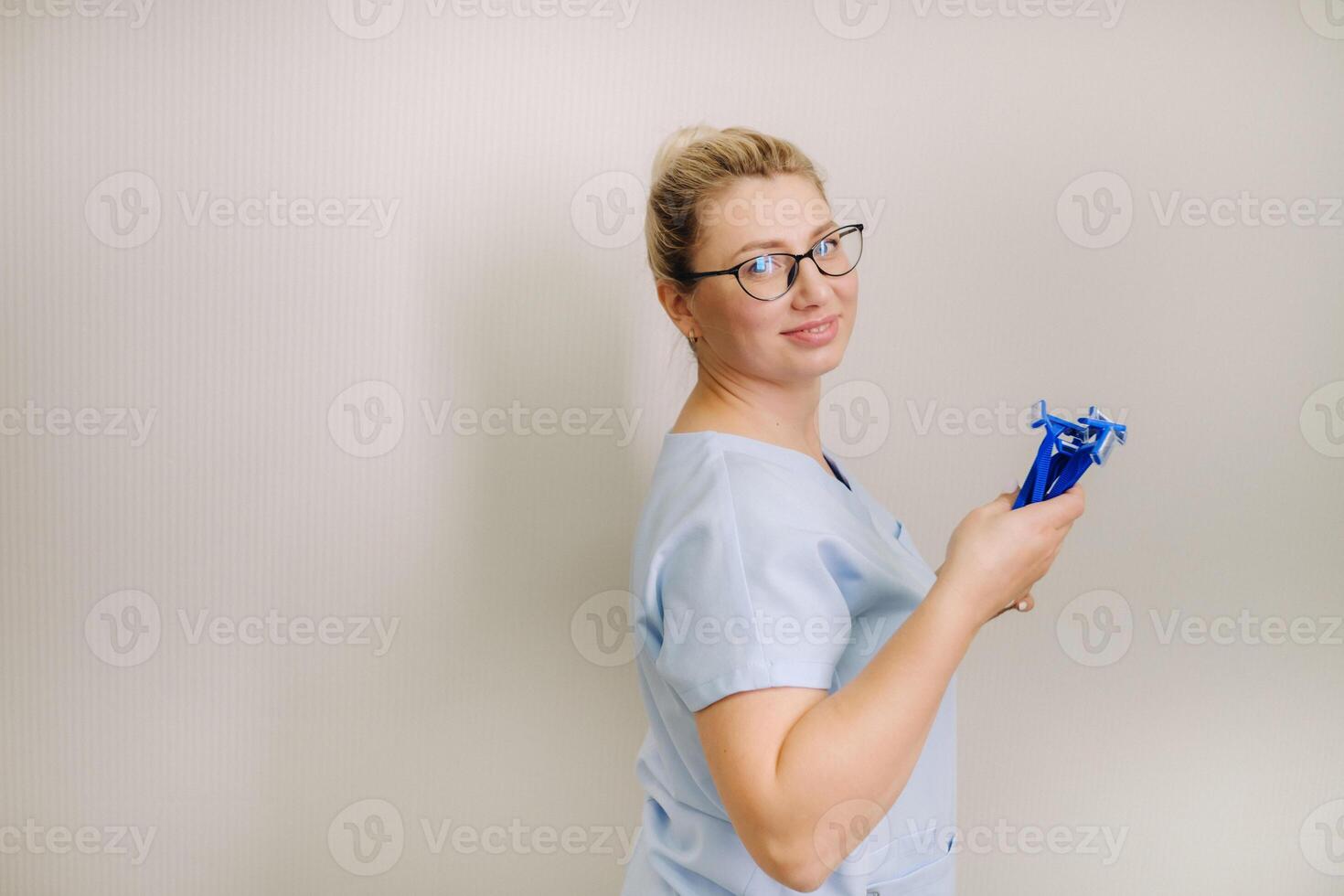 a female laser hair removal master in a blue robe holds shaving machines on a light background photo