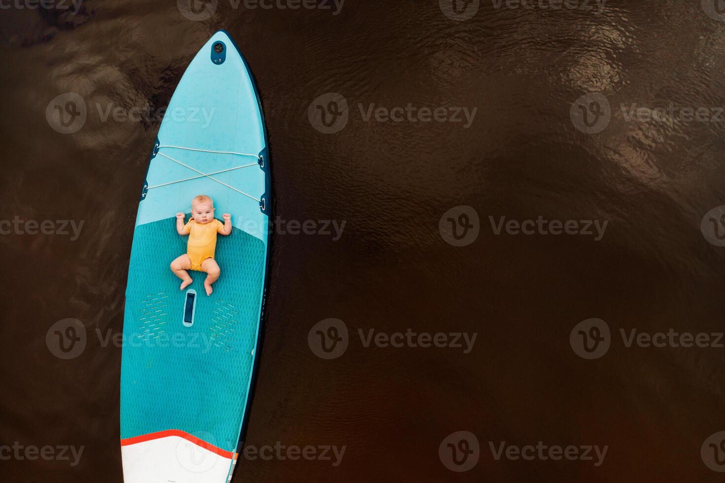 The child lies floating on the water on a large sup board. Water sports photo