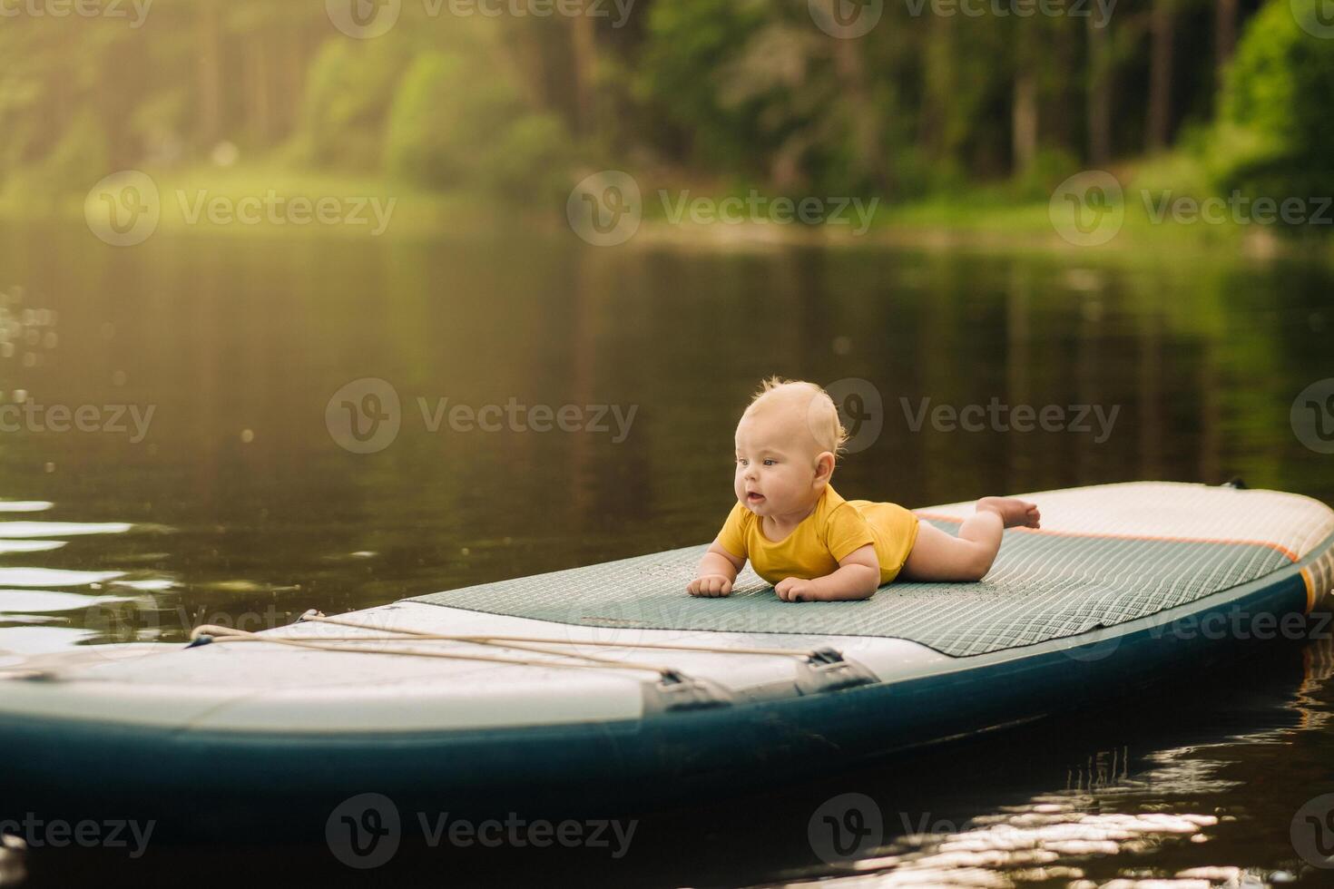 The child lies floating on the water on a large sup board. Water sports photo