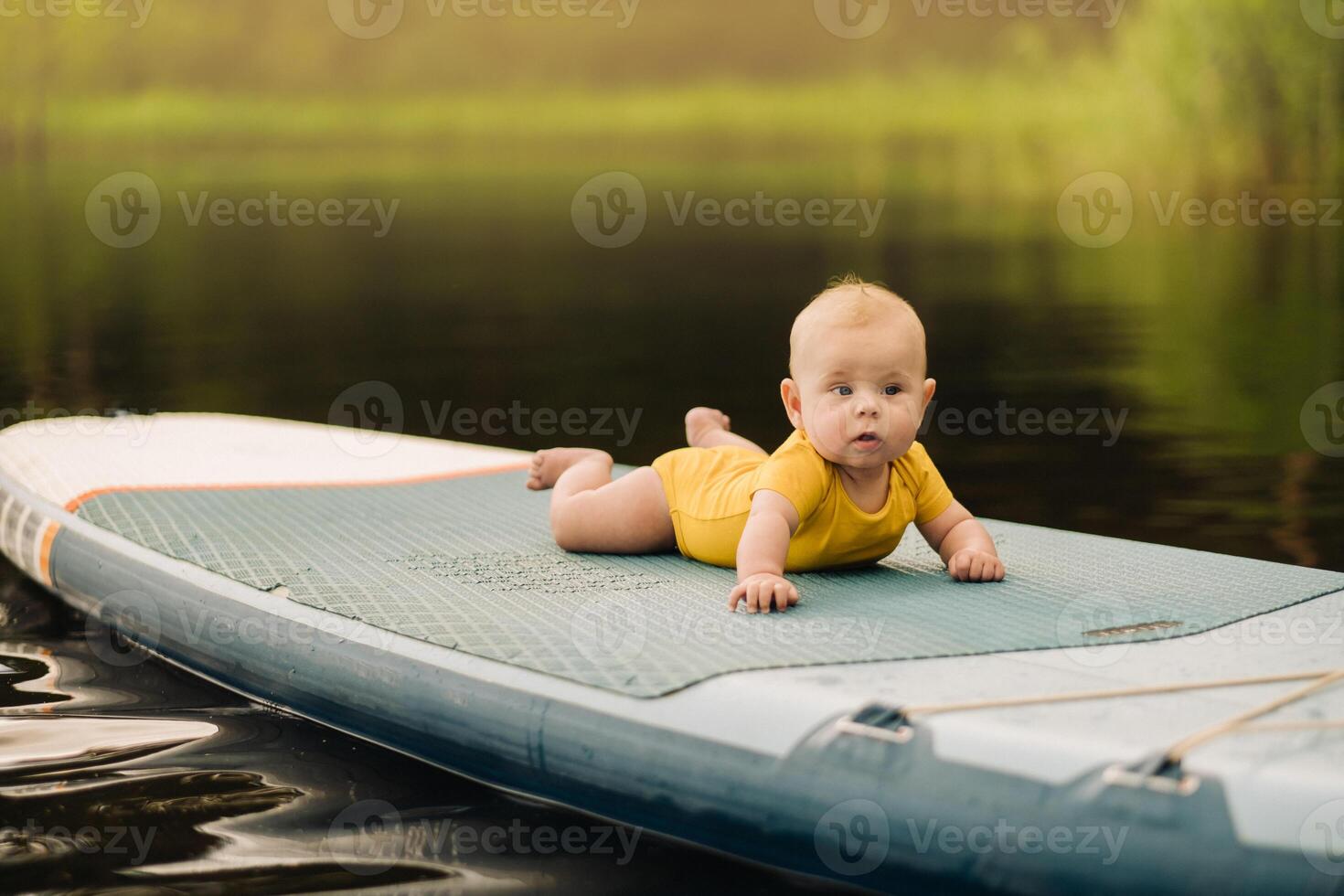 The child lies floating on the water on a large sup board. Water sports photo
