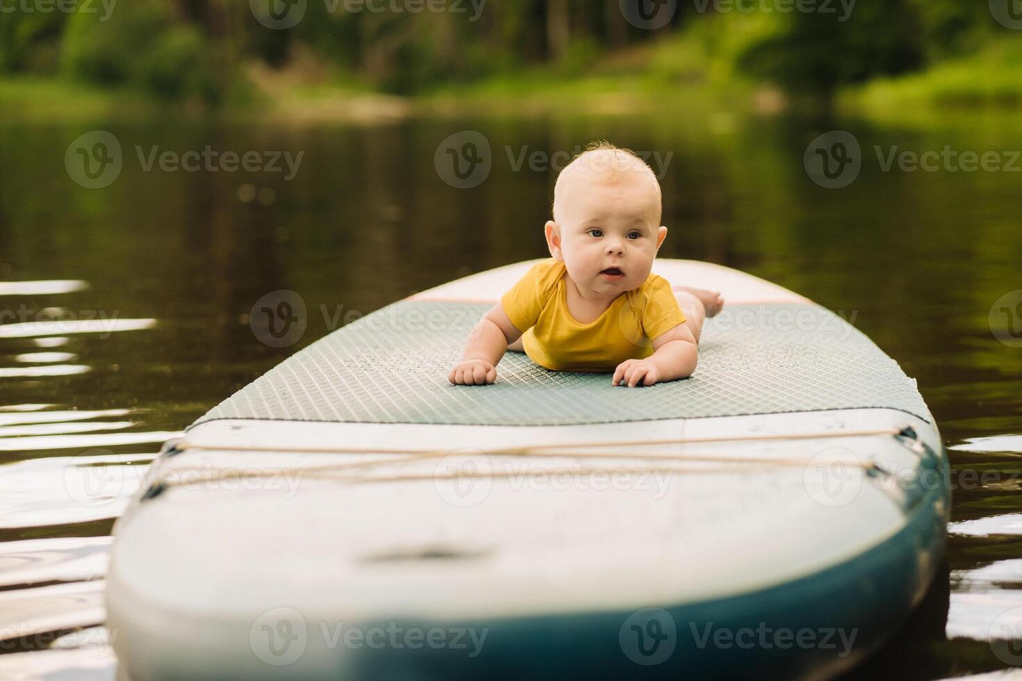 The child lies floating on the water on a large sup board. Water sports photo