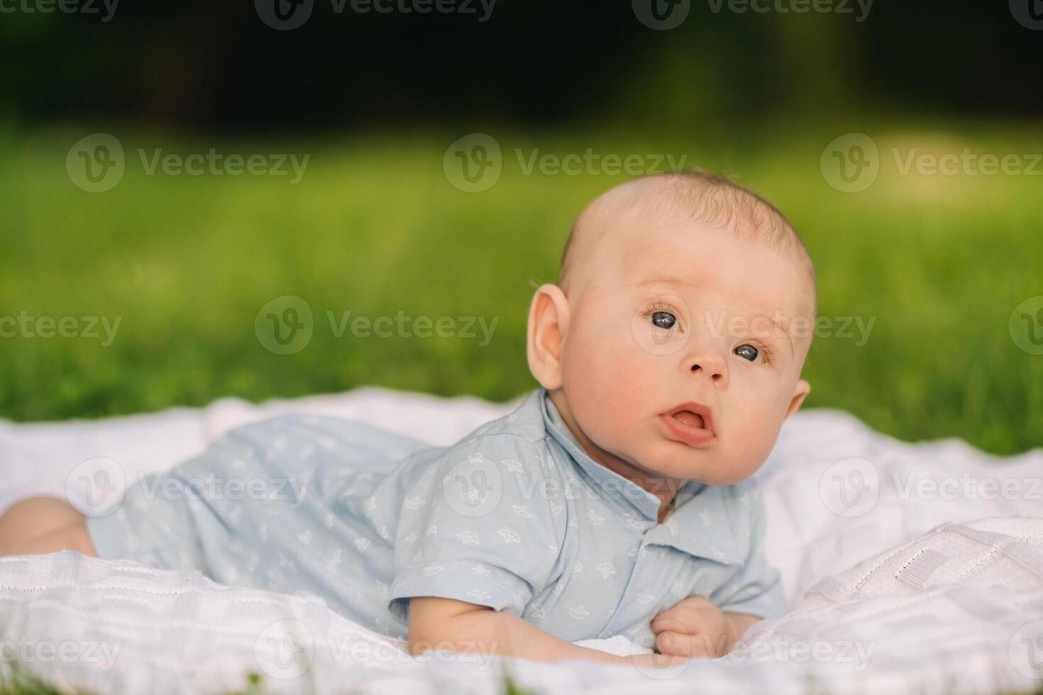 Cute happy toddler lying on a blanket on the grass outdoors in summer photo