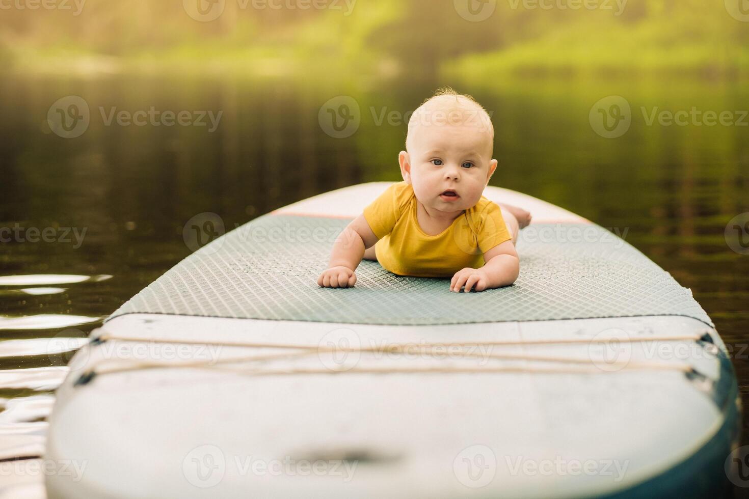 The child lies floating on the water on a large sup board. Water sports photo