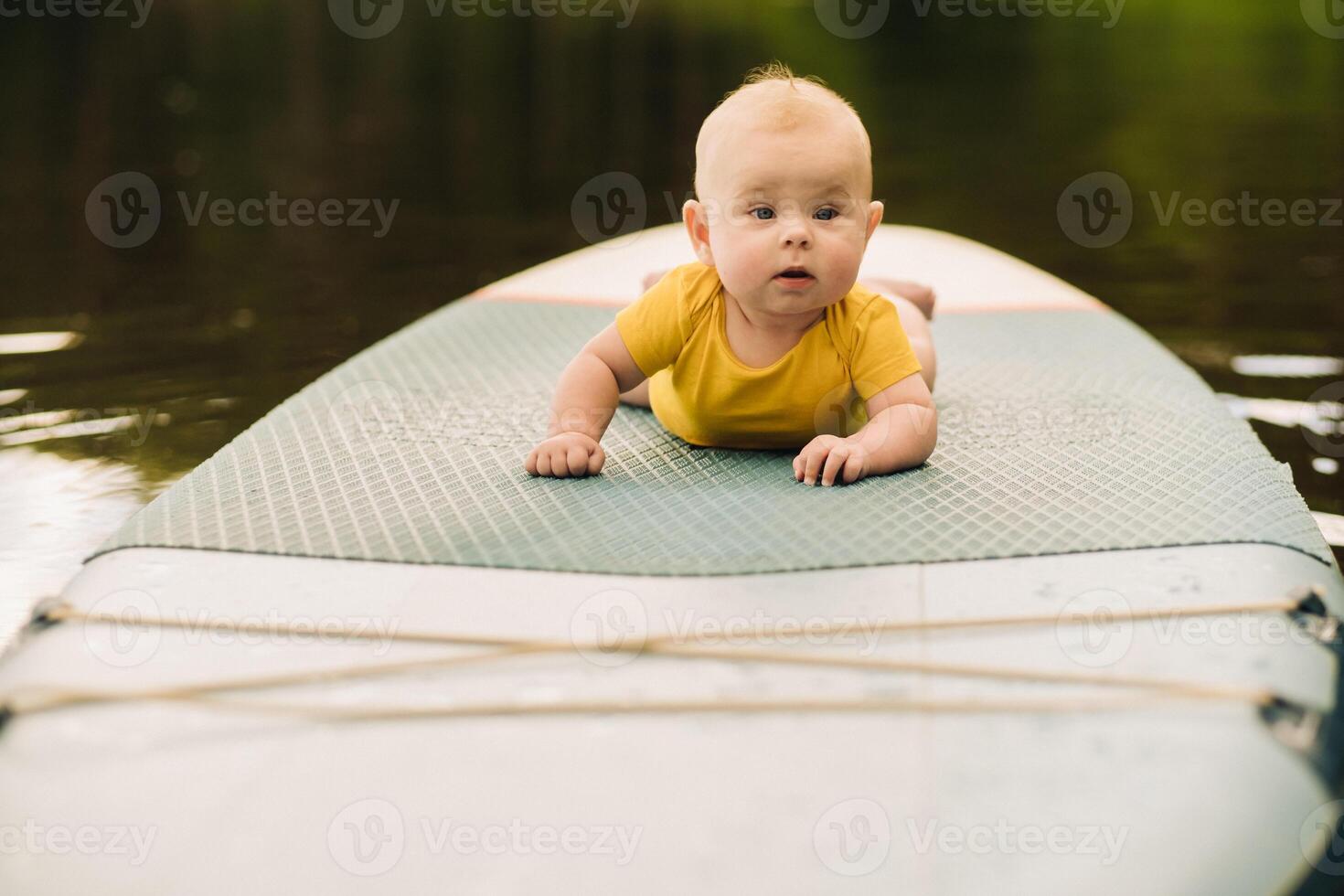The child lies floating on the water on a large sup board. Water sports photo