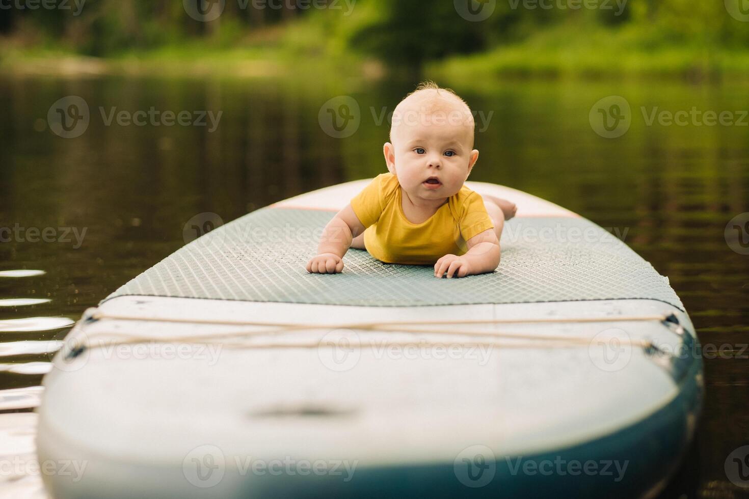 The child lies floating on the water on a large sup board. Water sports photo