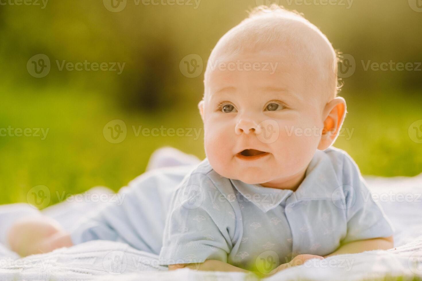 Cute happy toddler lying on a blanket on the grass outdoors in summer photo