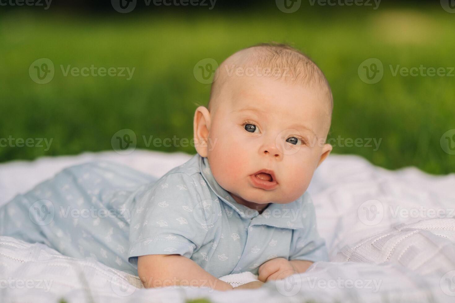 Cute happy toddler lying on a blanket on the grass outdoors in summer photo
