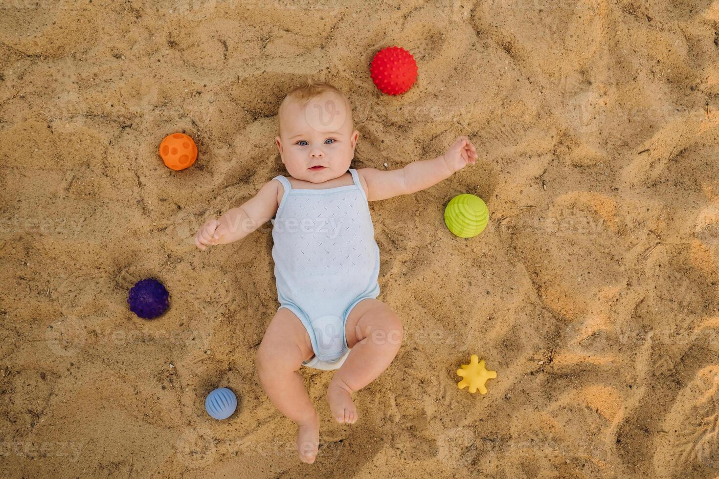 Top view of a happy little boy lying on a sandy beach photo