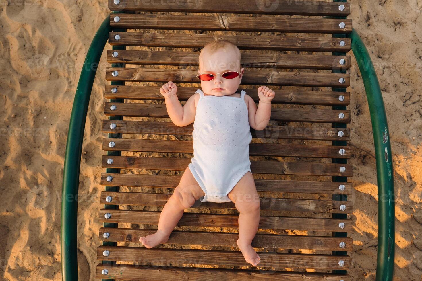 Top view of a happy little boy with glasses lying on a wooden sunbed photo