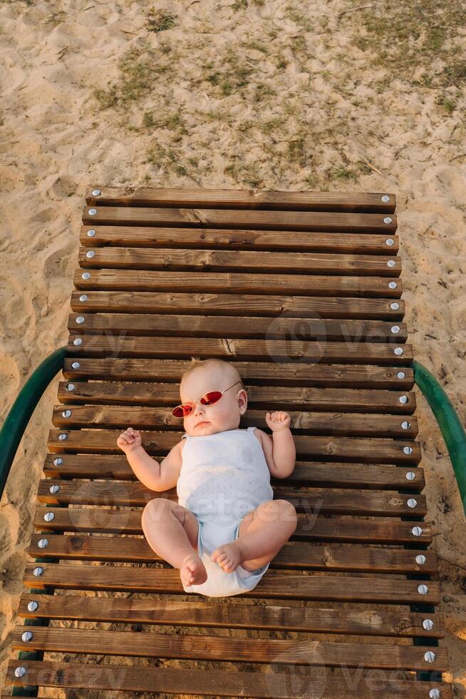 Top view of a happy little boy with glasses lying on a wooden sunbed photo