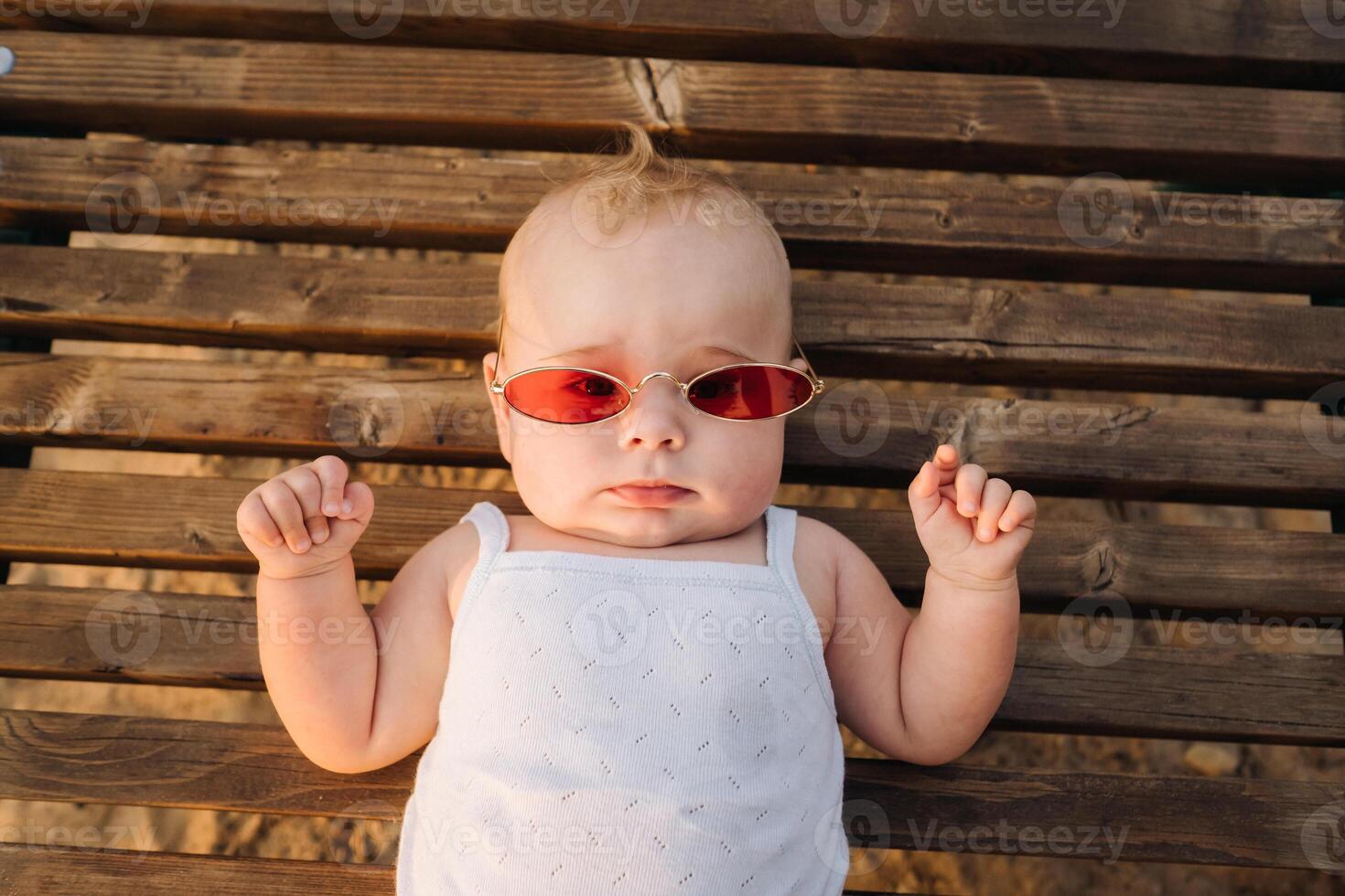 Top view of a happy little boy with glasses lying on a wooden sunbed photo