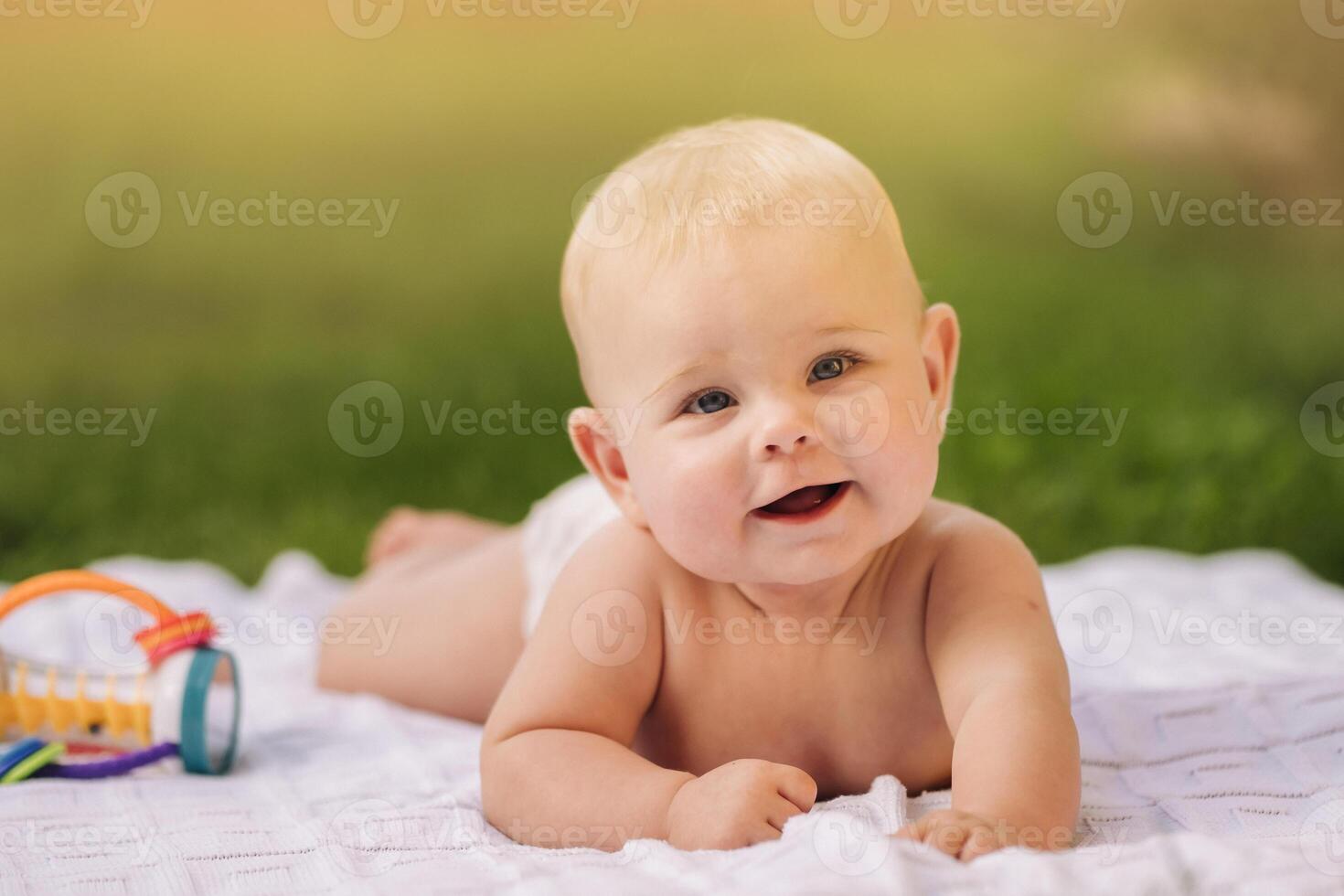 Cute happy toddler lying on a blanket on the grass outdoors in summer photo