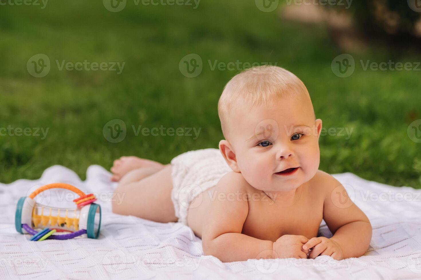 Cute happy toddler lying on a blanket on the grass outdoors in summer photo