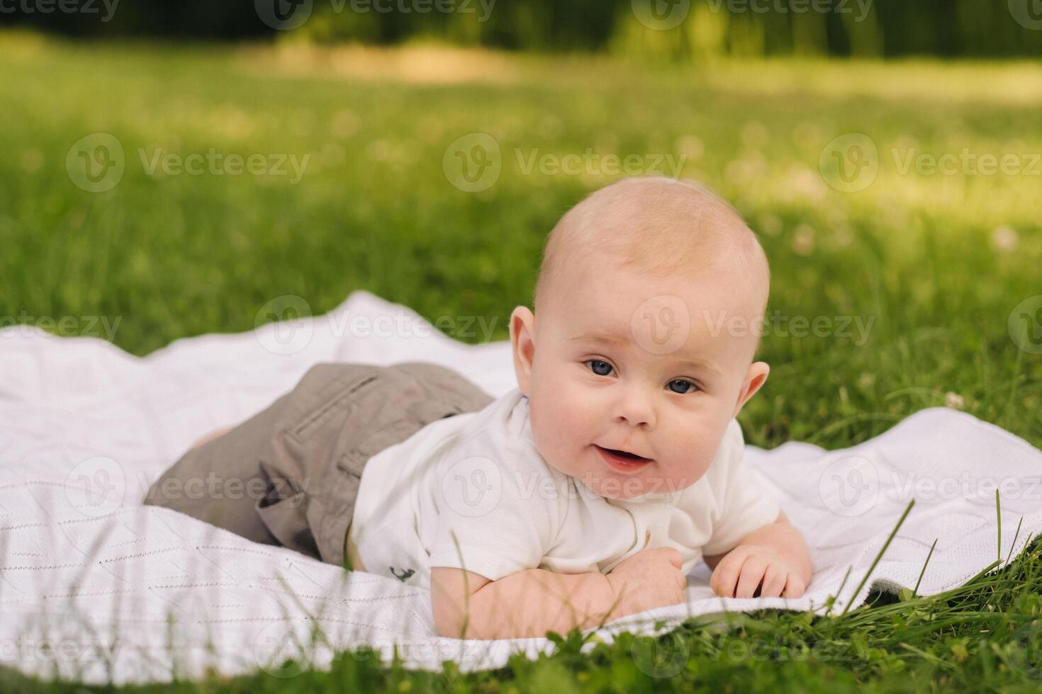 Cute happy toddler lying on a blanket on the grass outdoors in summer photo