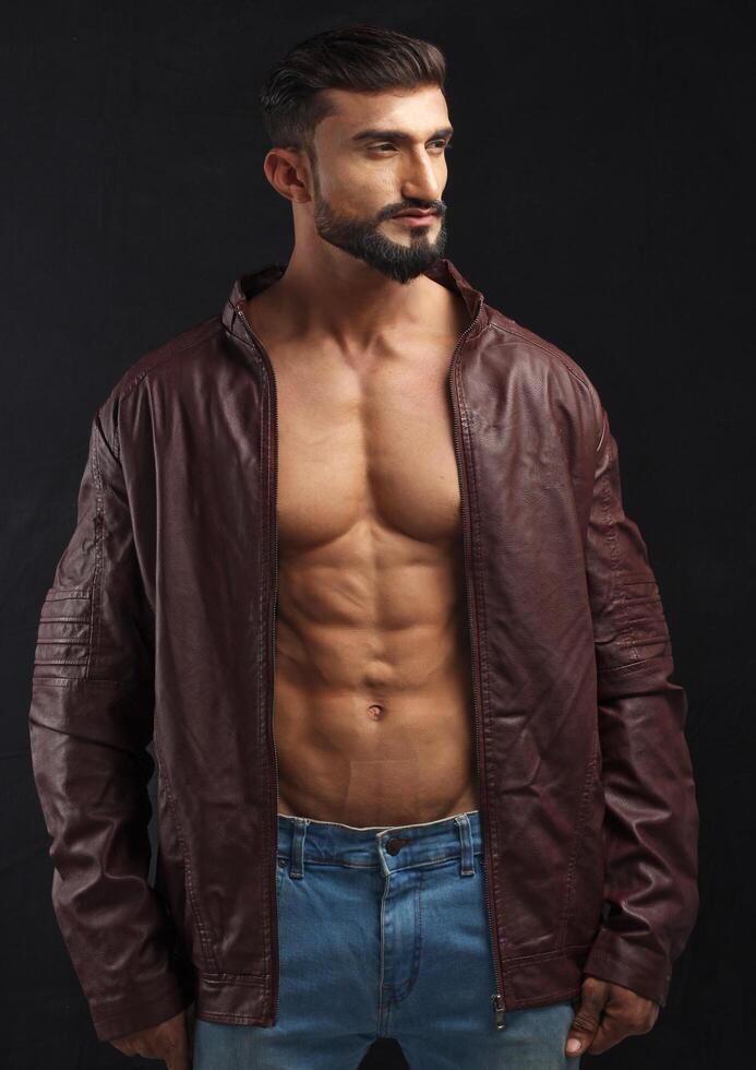 portrait of a young pakistani gym fit male model showing his build physique bicep triceps arms shoulder wings along with brown jacket photo
