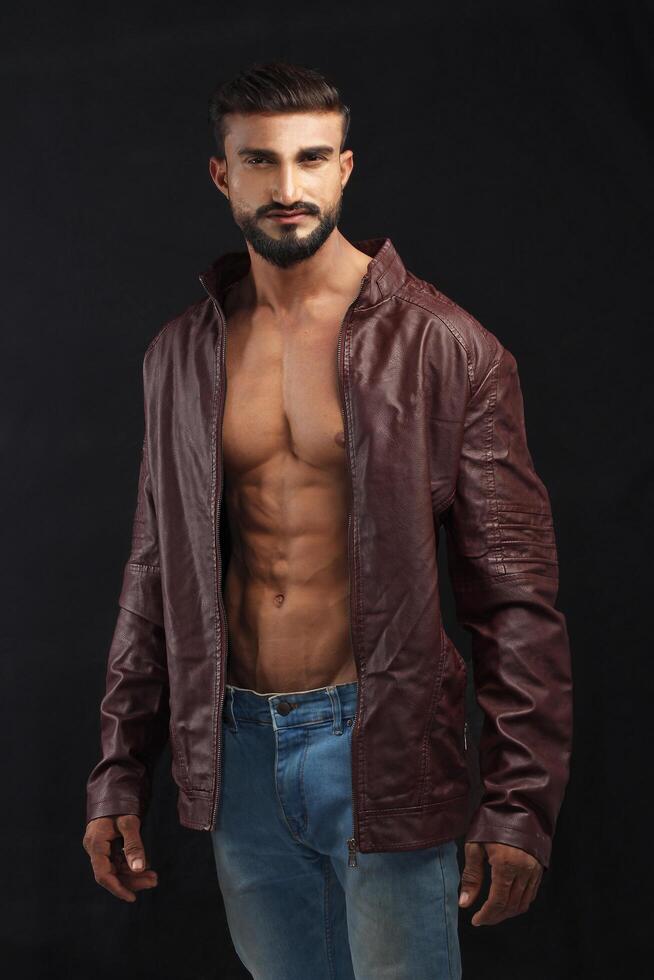 portrait of a young pakistani gym fit male model showing his build physique bicep triceps arms shoulder wings along with brown jacket photo