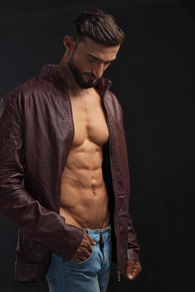 portrait of a young pakistani gym fit male model showing his build physique bicep triceps arms shoulder wings along with brown jacket photo