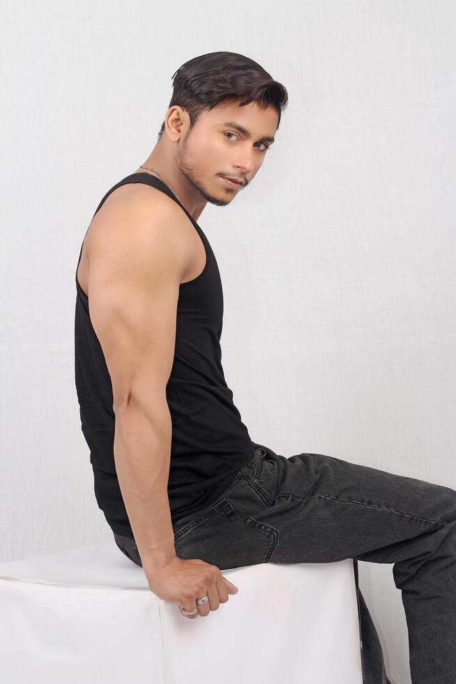 pakistani young man in black tank top sitting on a white box photo