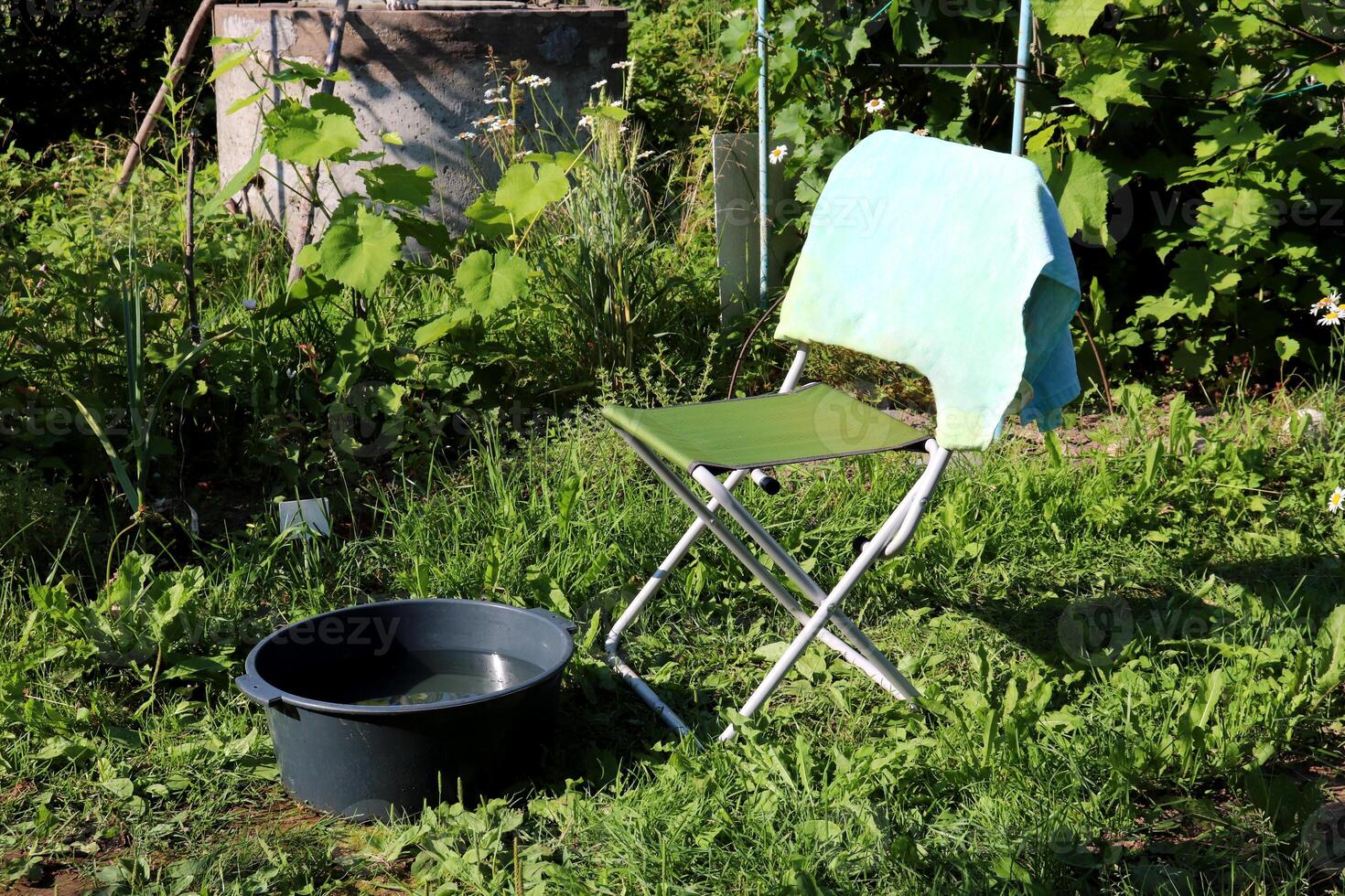 Folding chair and a plastic basin with water against the background of a round stone well photo