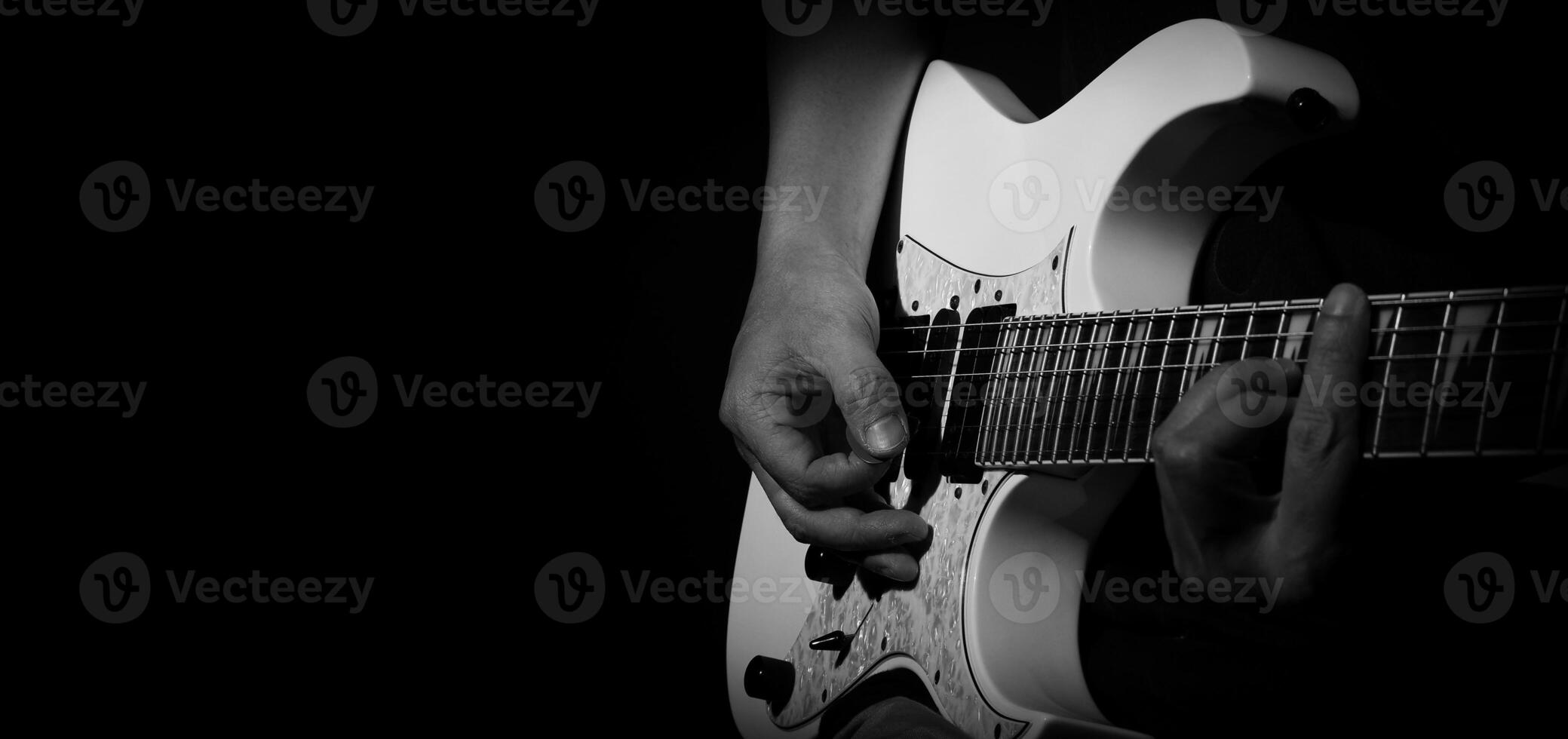 Guitarist Playing Guitar In Studio. Low key of man hand play white electric guitar for songs and cover music or skill practice. Close up of musician playing guitars instrument against black background photo