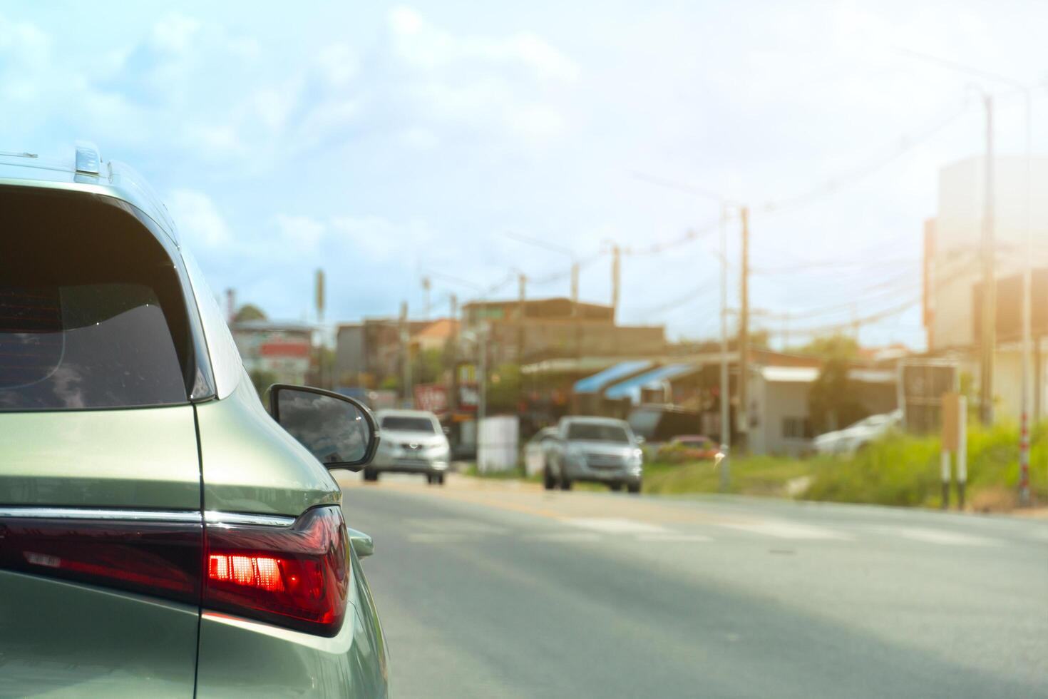 Rear side of car green pastel colors with turn on brake light. Driving on the aspahlt road with other cars opposits of road. Blurred background of small town under the sky. photo