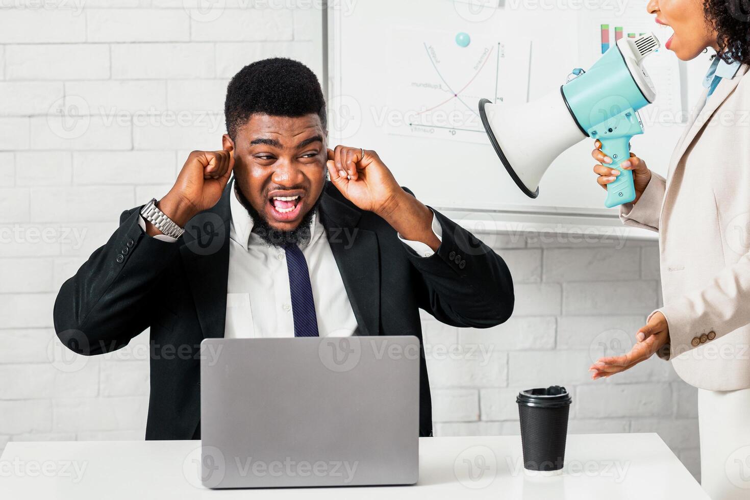 Enraged female boss with loudspeaker screaming at her scared subordinate at company office. Frightened male worker closing his ears, black businesswoman with megaphone yelling at him at workplace photo