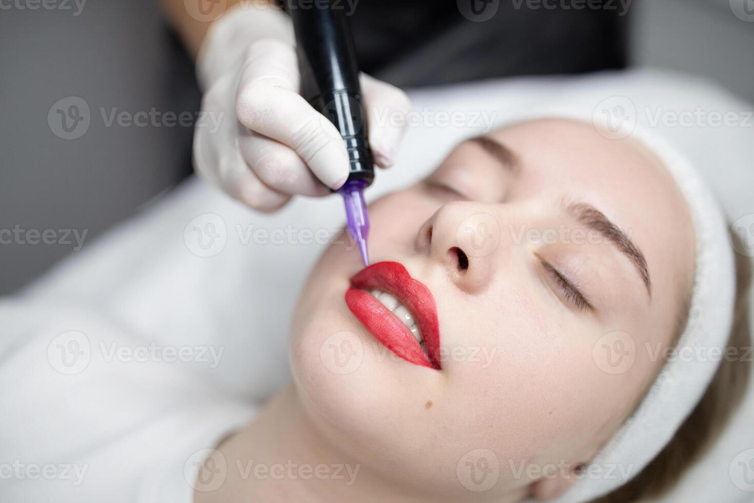 A woman relaxes in a beauty salon during a permanent makeup session. A skilled technician carefully applies pigment to enhance her lips, ensuring a pampering experience. photo
