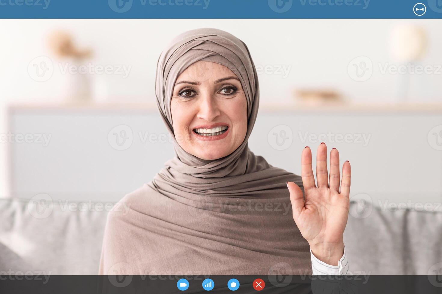 Hello. Cheerful Senior Woman In Hijab Waving Hand Gesturing Hi Greeting To Camera Sitting On Couch At Home. Call, Modern Distance Communication Concept. Panorama photo