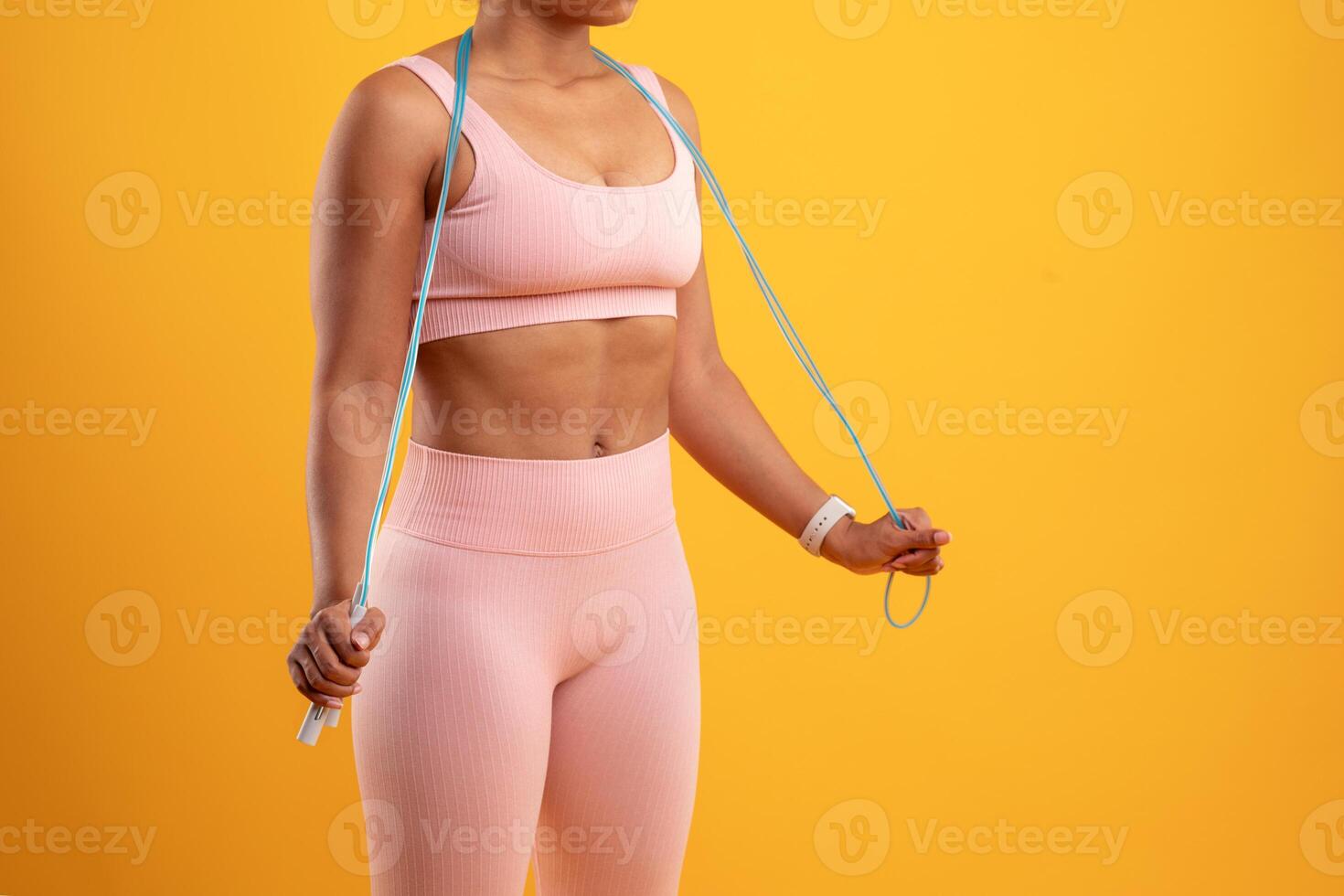 A person wearing a pink workout outfit stands against a bright yellow backdrop, holding a jump rope and preparing for a home exercise session focused on fitness and health improvement. photo