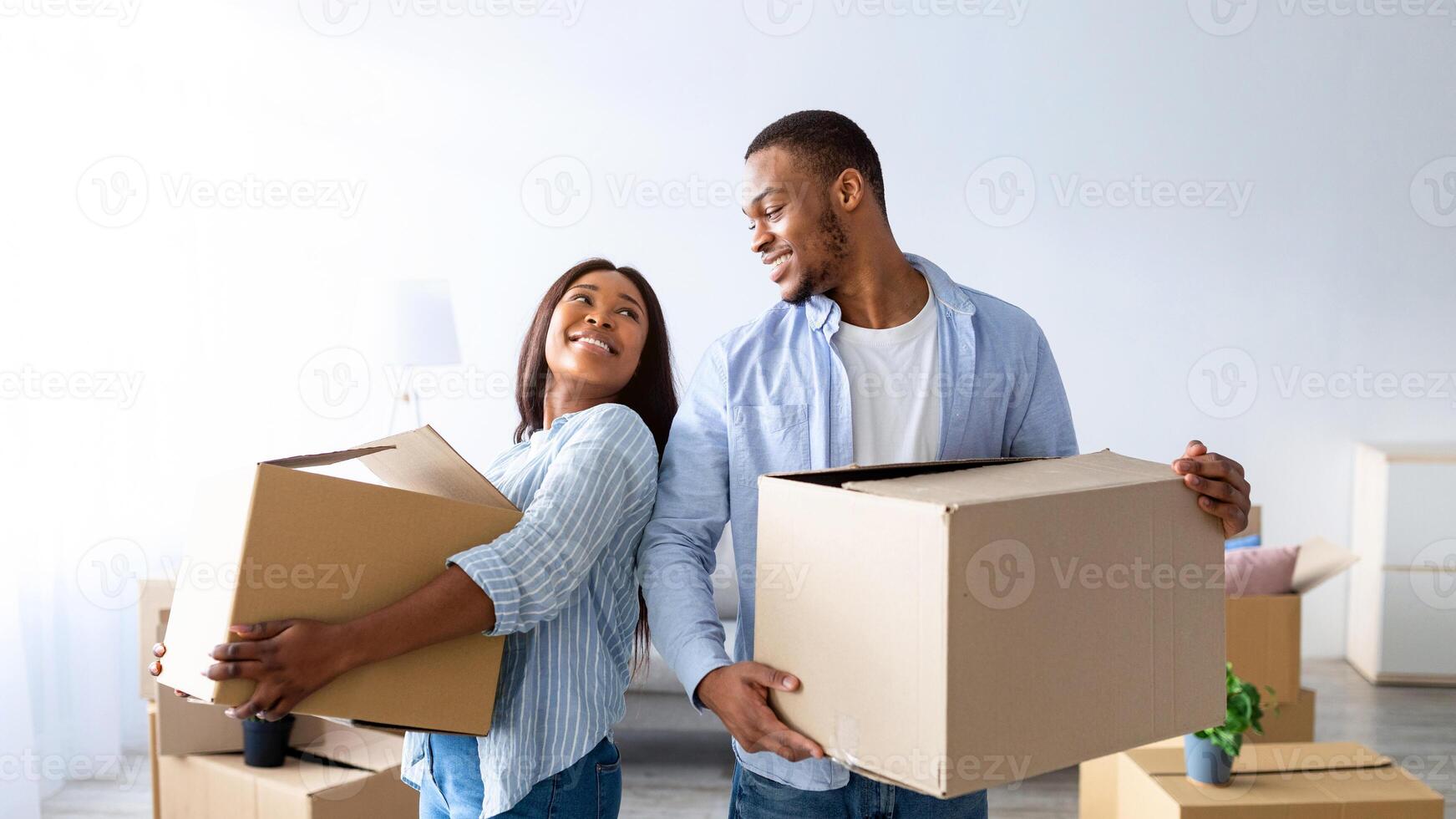 Home relocation concept. Loving african american couple carrying carton boxes in their new house, copy space. Young tenants with belongings moving into new property photo