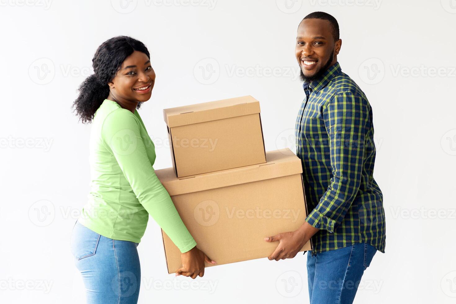 Home Relocation Concept. Joyful black spouses carrying cardboard boxes in their house, young african american couple holding belongings and smiling at camera while moving into new apartment photo