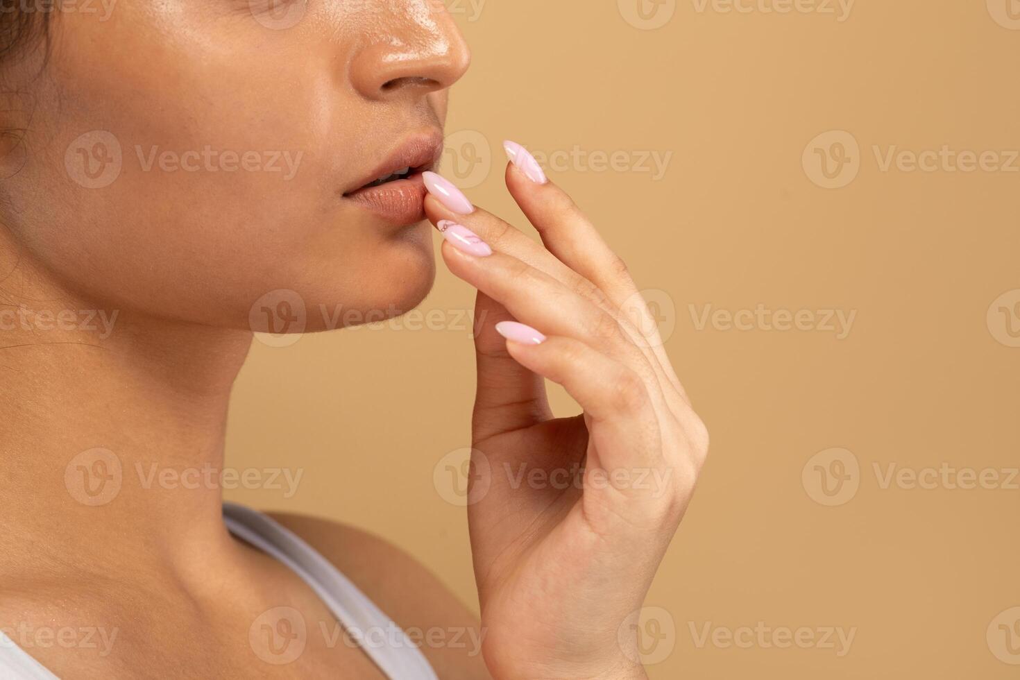 A young Indian woman focuses on her skin care routine, gently touching her lips with a thoughtful expression. She embodies beauty and self-care against a neutral backdrop, copy space photo