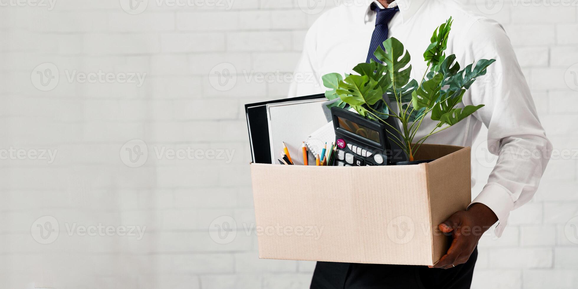 Losing job concept. Closeup view of African American guy with box of his stuff leaving office. Panorama photo