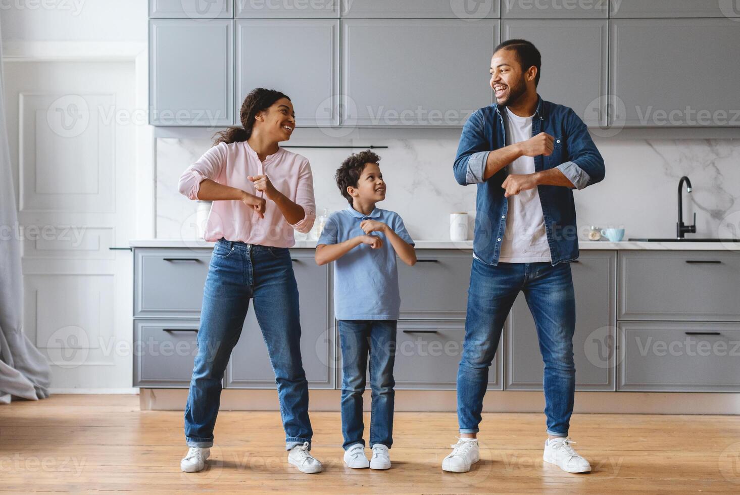 A joyful family shares a lively dance in their stylish kitchen. The parents and their son show affection and happiness, creating lasting memories in their home together. photo
