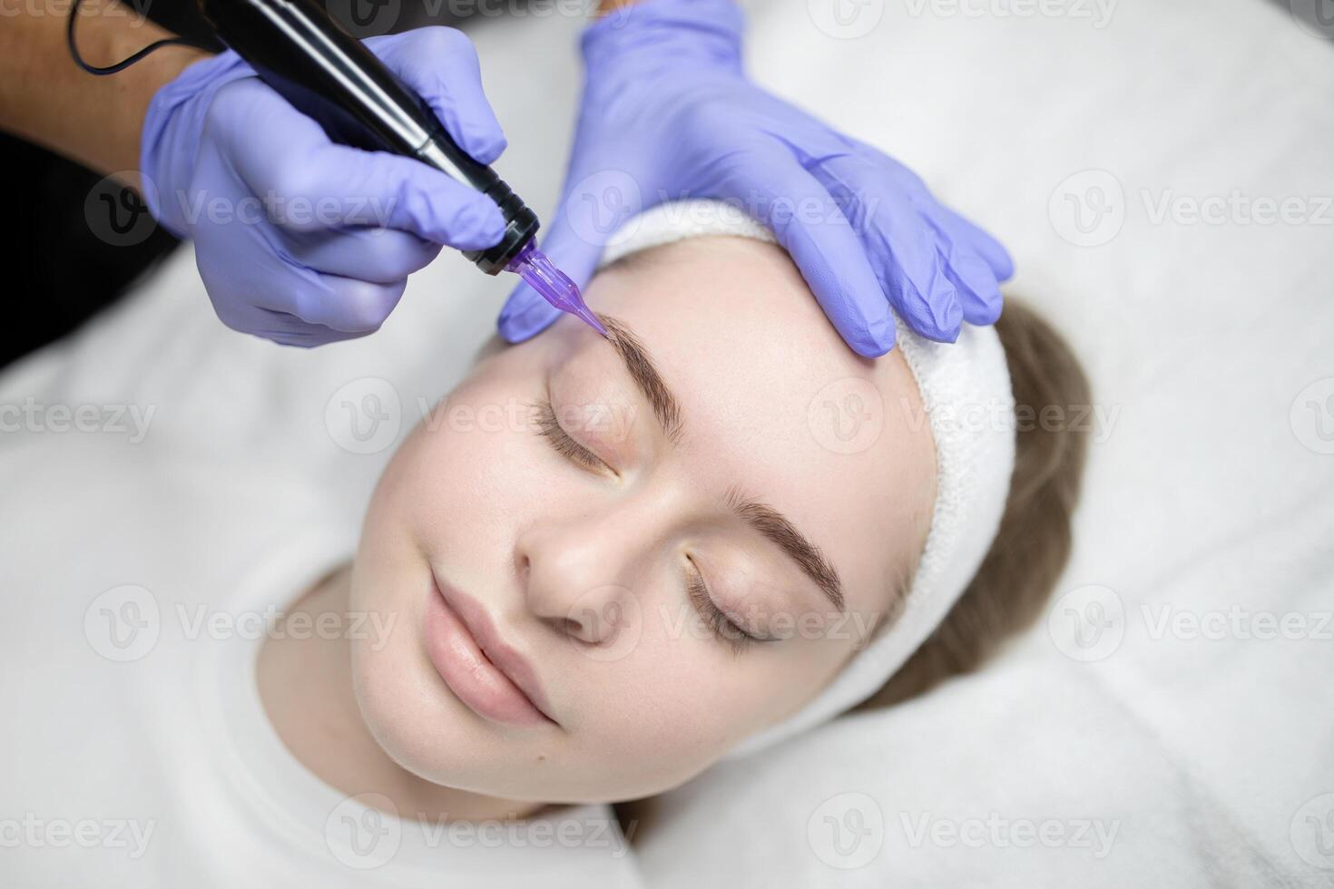 A woman relaxes in a beauty salon while receiving a permanent makeup procedure. The beautician skillfully applies makeup, enhancing the client natural beauty during this long-lasting session. photo