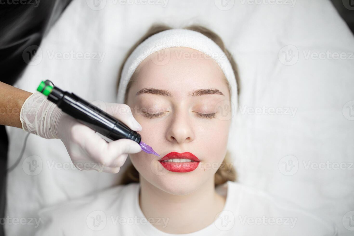 A woman enjoys a pampering session for permanent makeup at a beauty salon. The technician carefully applies a procedure with precision on her lips, enhancing her natural look. photo