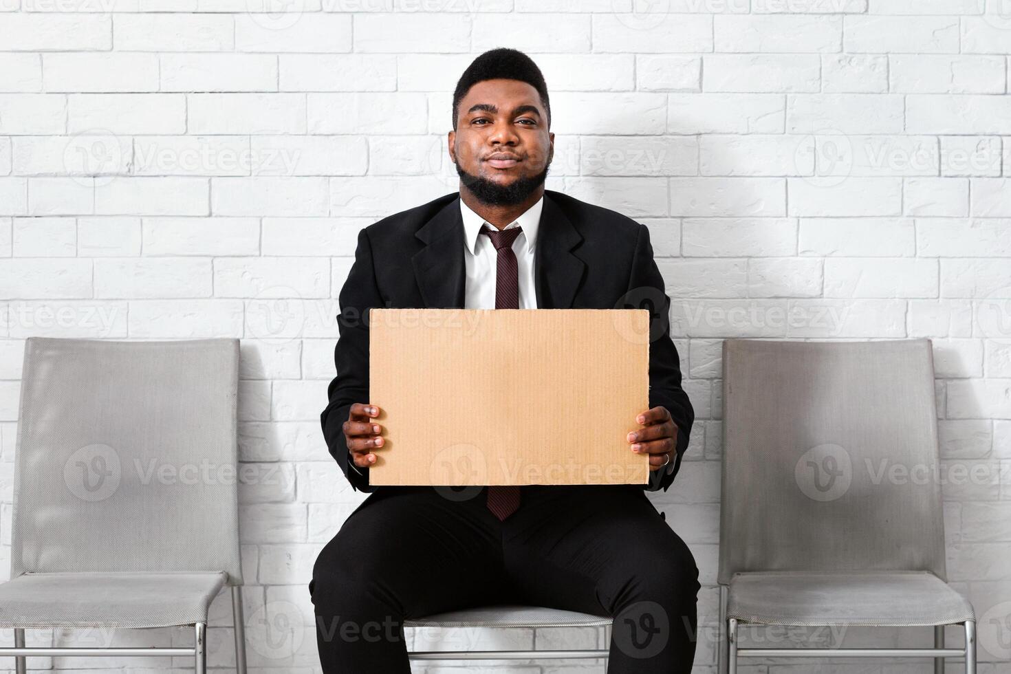 Serious black man in office wear holding blank sign in company hall, waiting for job interview. Copy space. Panorama photo