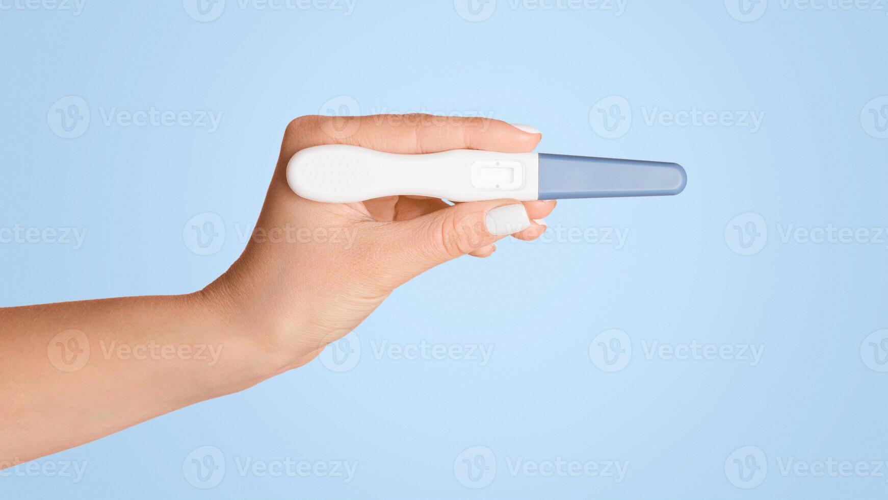 Unrecognizable woman holding blank pregnancy or ovulation test on pink background, closeup view. Copy space photo