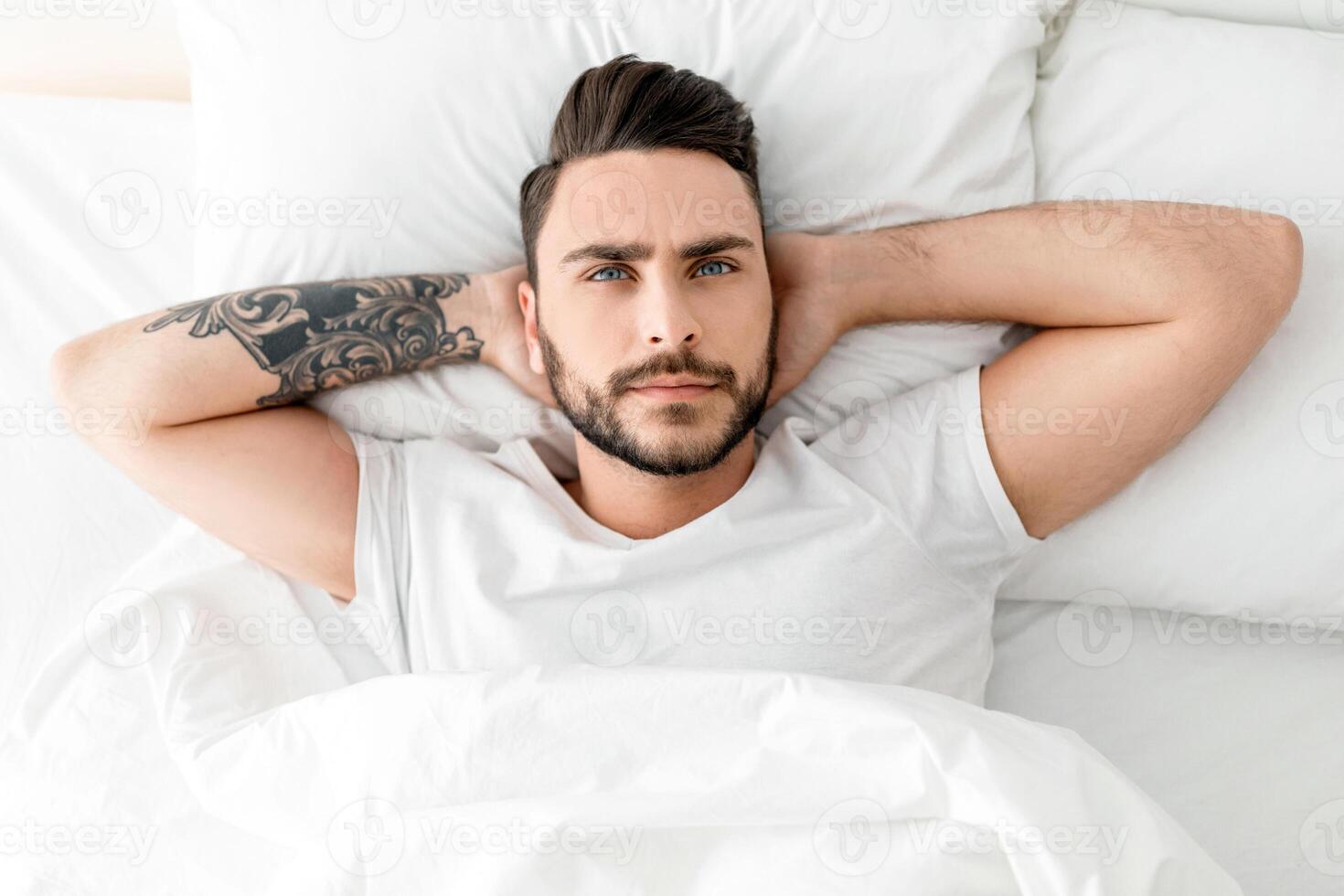 Depressed young man unable to sleep, lying in bed, looking up and contemplating, top view. Sleeplessness, mental health problem, male depression concept photo