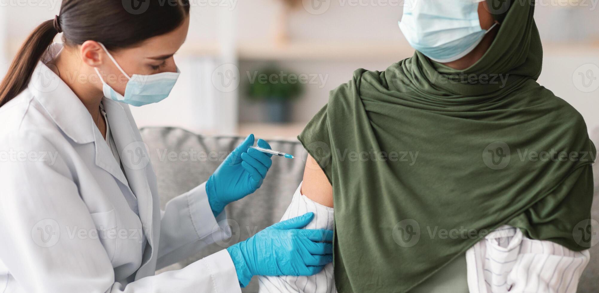 Coronavirus Vaccination, Immunization. Unrecognizable Muslim Lady Getting Vaccinated Against Covid-19, General Practitioner Injecting Vaccine With Syringe In Arm Indoors. Antiviral Protection photo