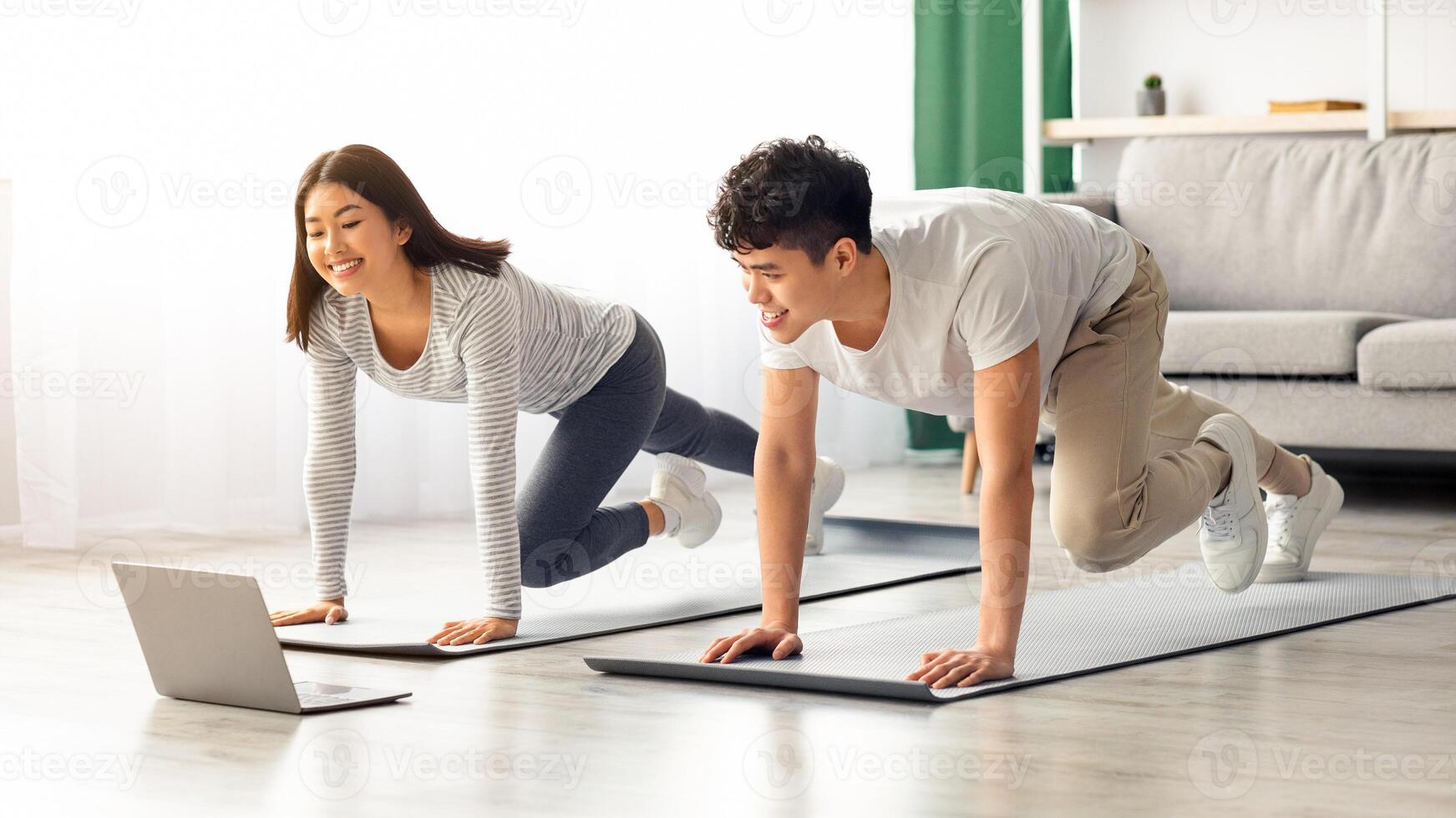 Athletic asian family exercising together at home, stretching on fitness mat, looking at laptop screen, having online class, living room interior, copy space. Sporty black couple training together photo