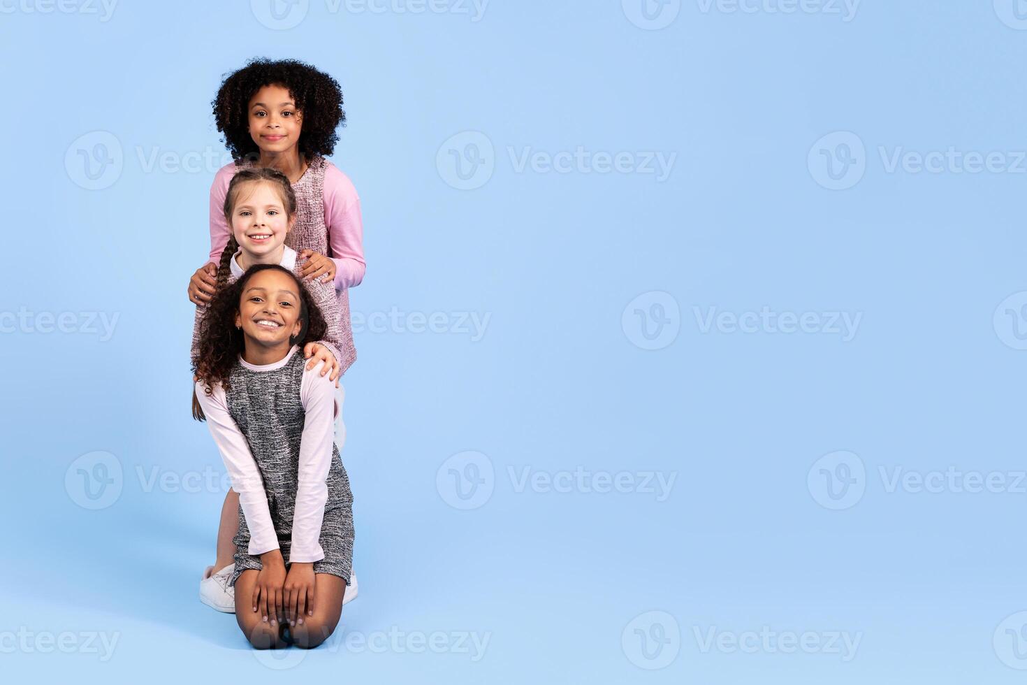 Three joyful girls of different backgrounds are posing together in playful harmony. They are smiling and showcasing a connection that celebrates childhood joy and friendship, copy space photo