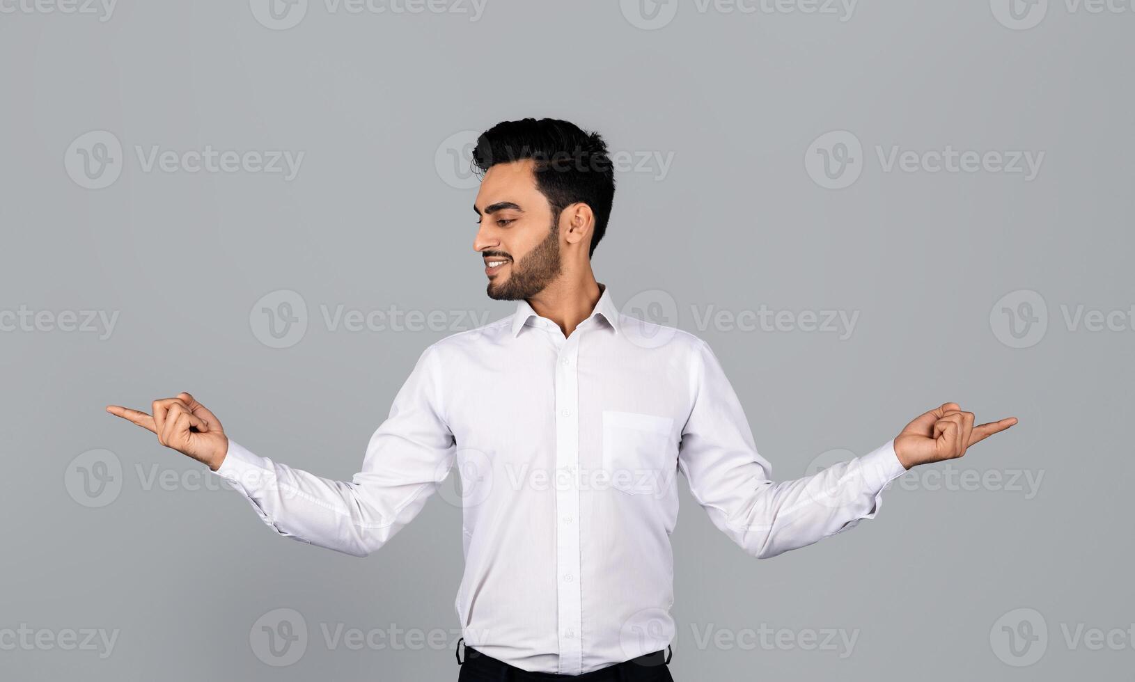 A Middle Eastern businessman stands confidently in a studio environment, gesturing with both hands. He radiates professionalism and youthful energy, embodying a modern entrepreneurial spirit. photo