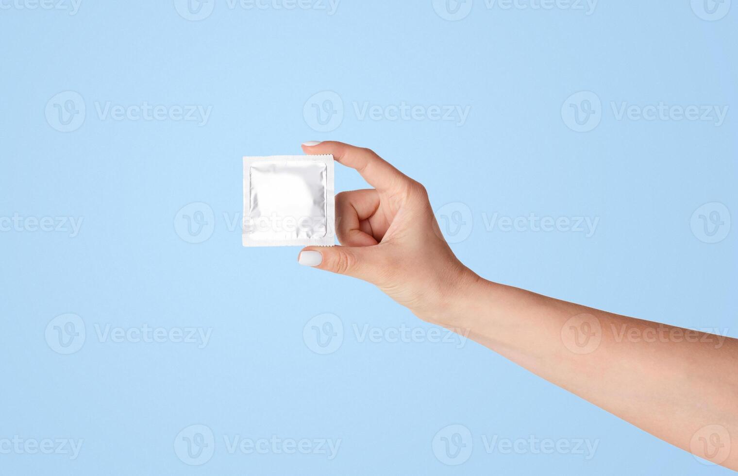 Safe sex. Millennial girl showing condom with wrapper on light background, close up of hand. Panorama photo