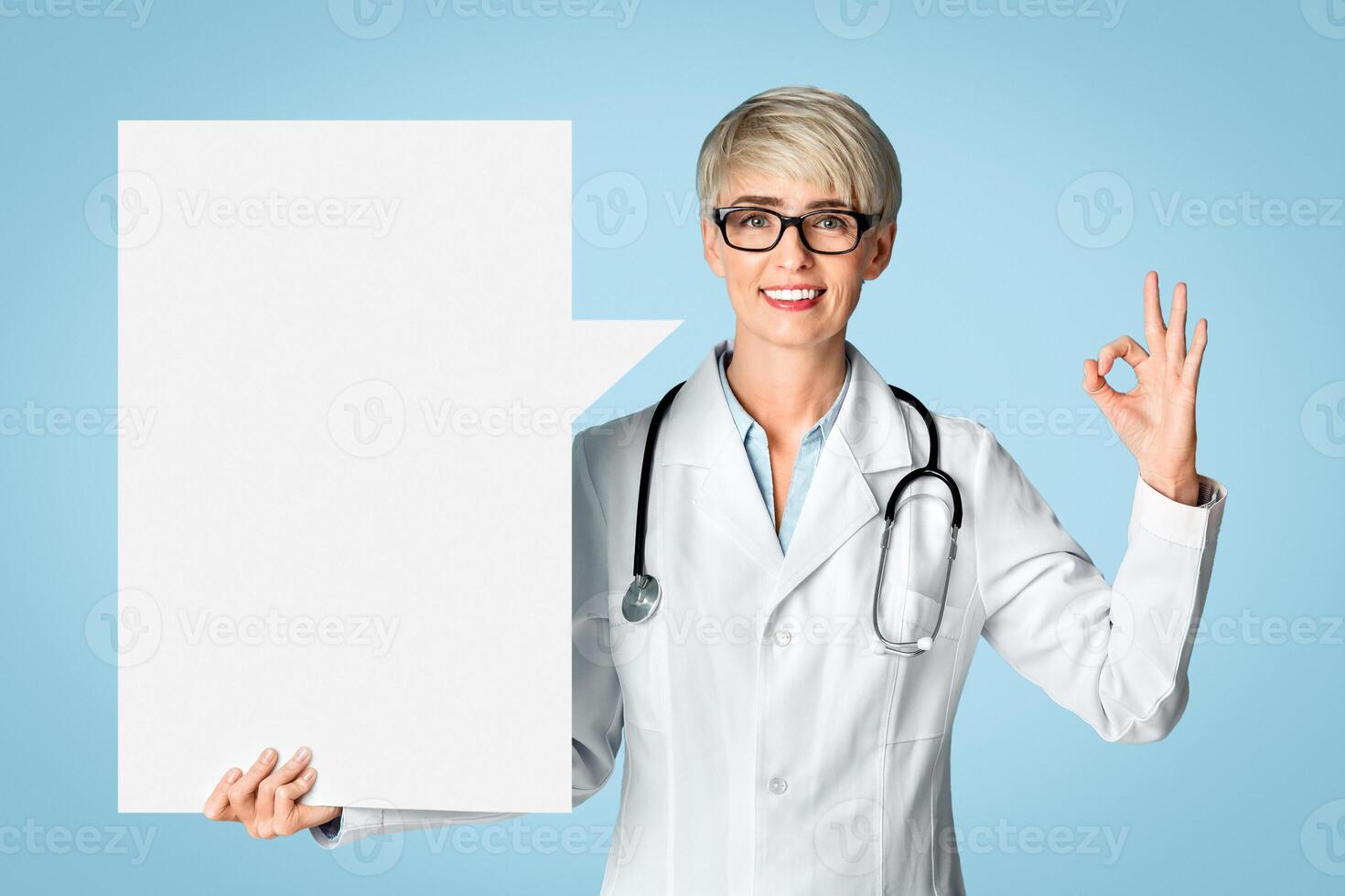 Excellent doctor recommendation. Smiling Woman in white coat shows ok sign with abstract place for words isolated on blue background, studio shot photo