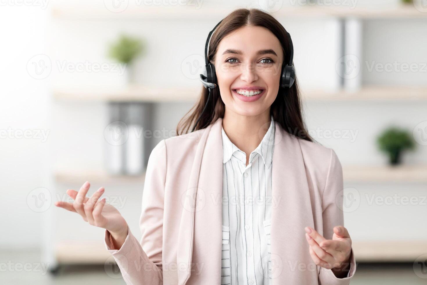 Portrait Of Hotline Operator Lady Wearing Headset Smiling And Talking Looking At Camera Standing In Modern Office. Call, Online Consultation With Professional Consultant Or Manager Concept photo