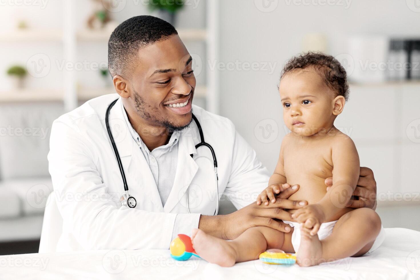 Medical Care For Babies. Smiling Black Pediatrician Making Health Check Up For Little Baby Patient In Clinic, Friendly African American Doctor Having Appointment With Cute Infant Child, Closeup photo