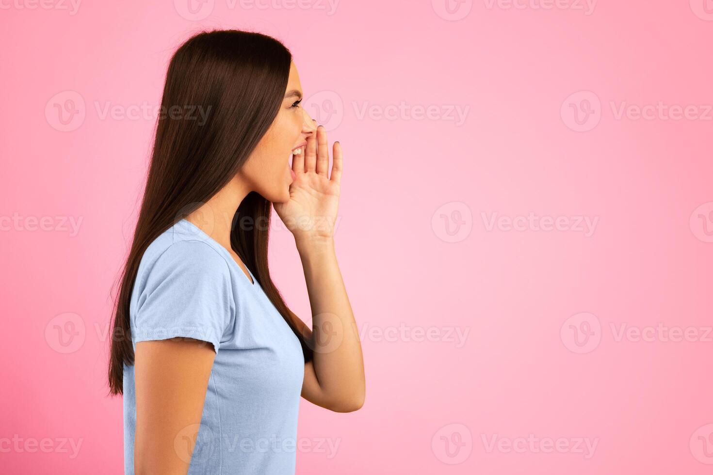 Making Announcement. Closeup side view portrait of emotinal woman shouting and holding palm near mouth. Female model screaming important information at copy space isolated on yellow studio background photo
